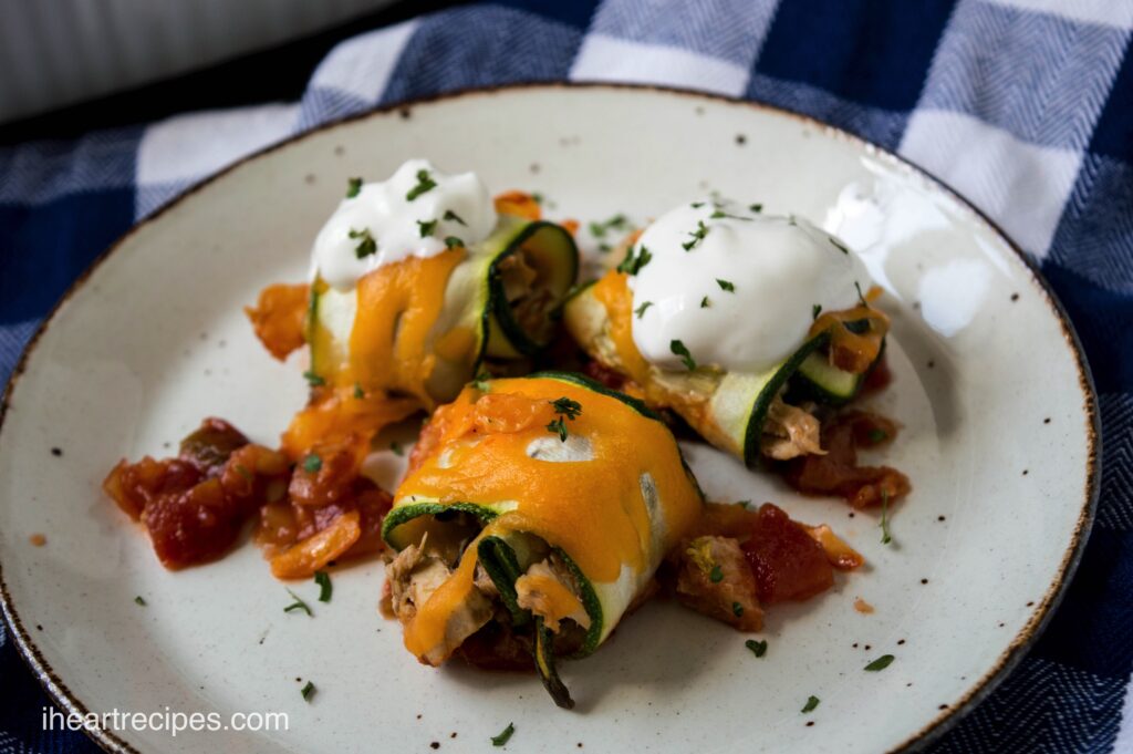 Three cheesy zucchini chicken taco rolls arranged on a white plate on top of a blue and white table cloth.