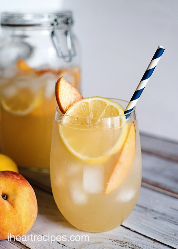 An ice-cold glass of homemade peach lemonade garnished with lemon and peach slices.