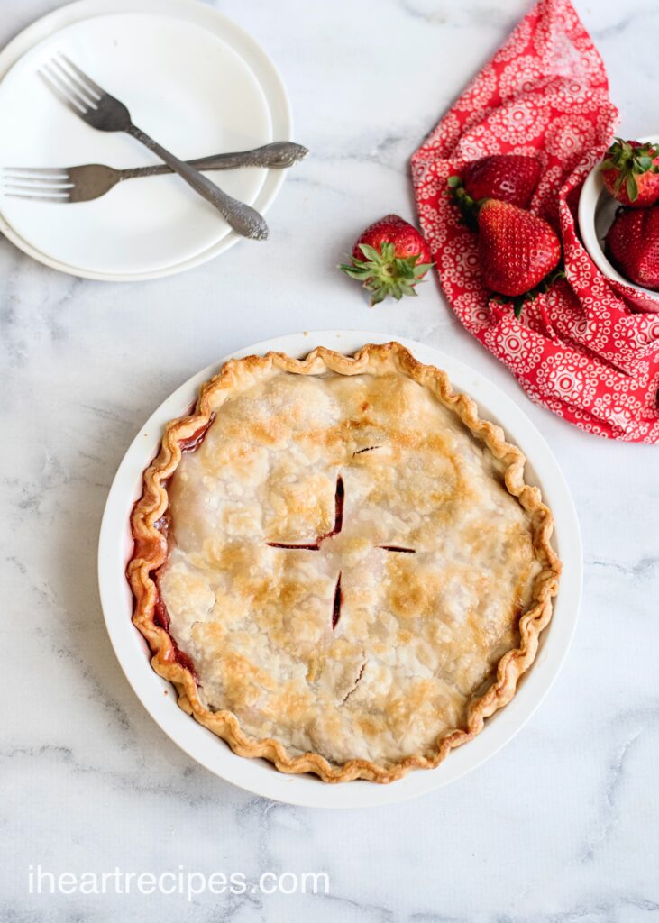 A fresh-baked homemade strawberry rhubarb pie in a white pie dish on a marble countertop.