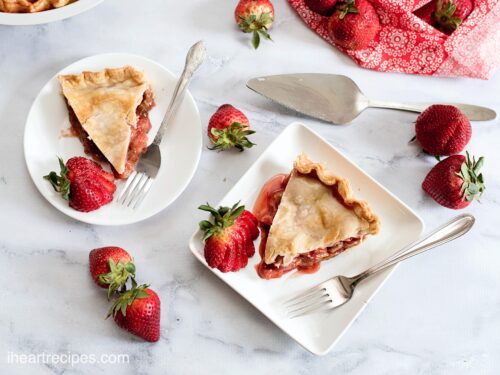 Slices of homemade strawberry rhubarb pie served on white plates with strawberries.