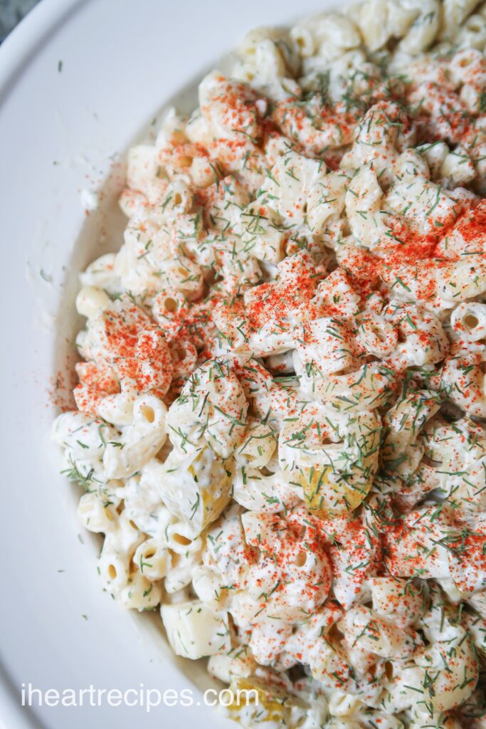 A bowl full of creamy macaroni pasta salad with a creamy dressing, cheese, topped with paprika and dill.