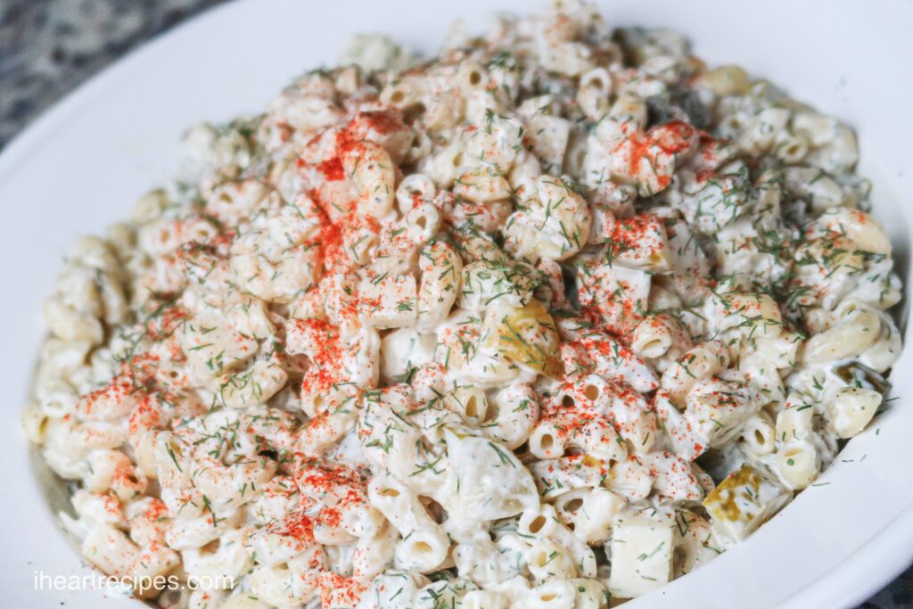 A creamy bowl filled with macaroni pasta salad, ranch dressing, cheese, garnished with paprika and dill.