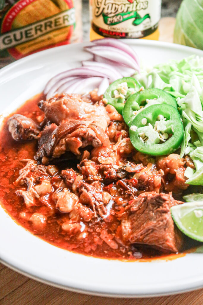 A closeup look at a hearty bowl of pork pozole with jalapeno and lime garnish.