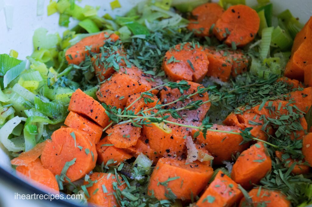 A mixture of chopped carrots, celery, leeks, and fresh herbs mixed together in a bowl.