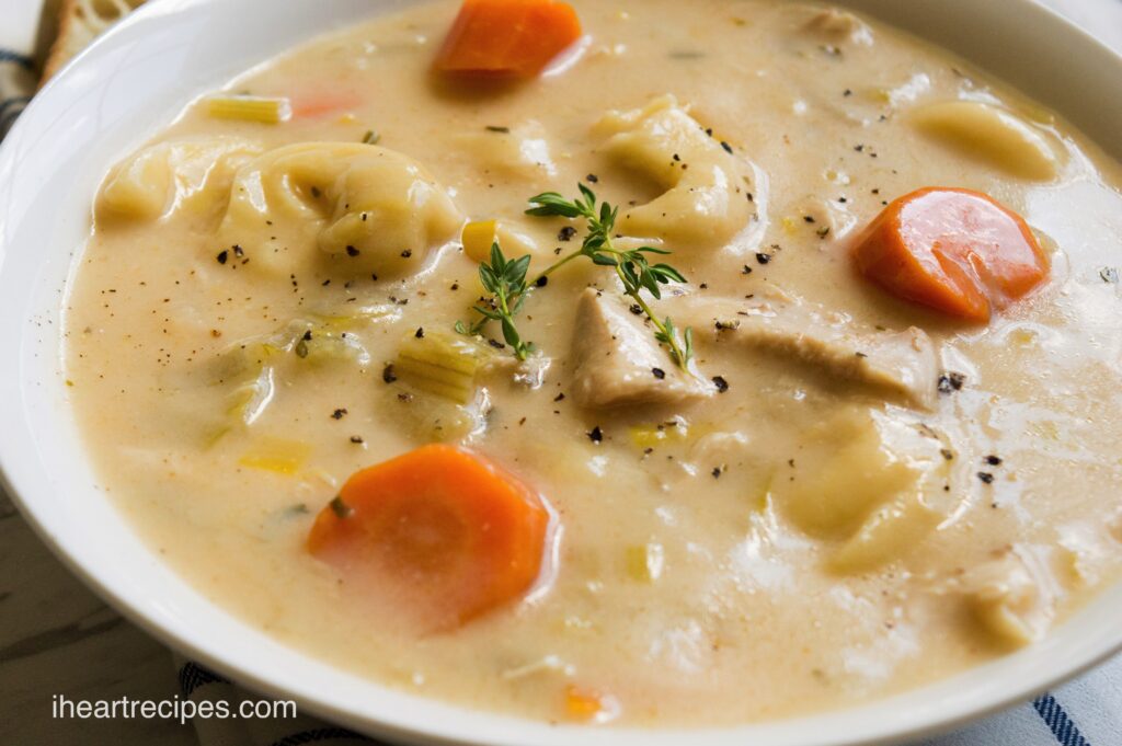 A large white bowl filled with creamy Chicken Tortellini soup, made with carrots, celery, chicken, and fresh herbs in a creamy broth.