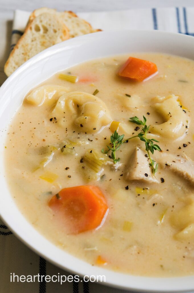 A close up image of a bowl of homemade Chicken Tortellini soup, with carrots, celery, and a fresh herb garnish.