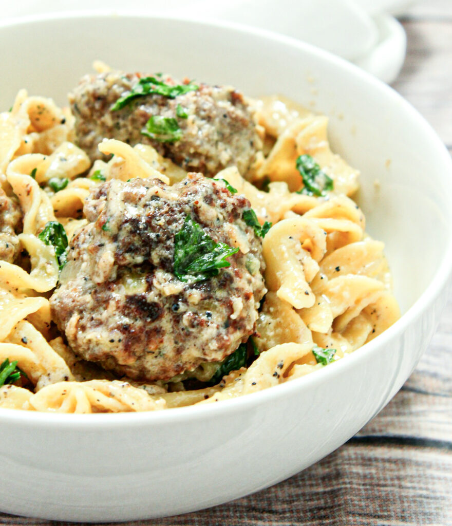 A bowl of Swedish meatballs and egg noodles, coated in a creamy gravy and topped with parsley and grated parmesan cheese.