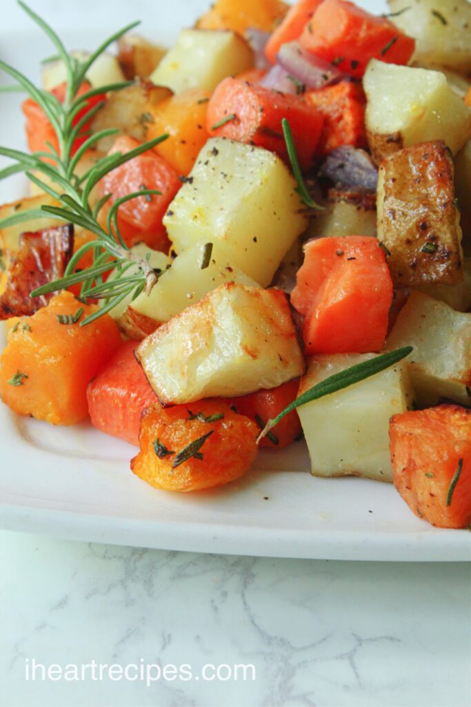 A golden mix of air fryer roast potatoes, squash and onions garnished with fresh rosemary leaves served on a white plate.  