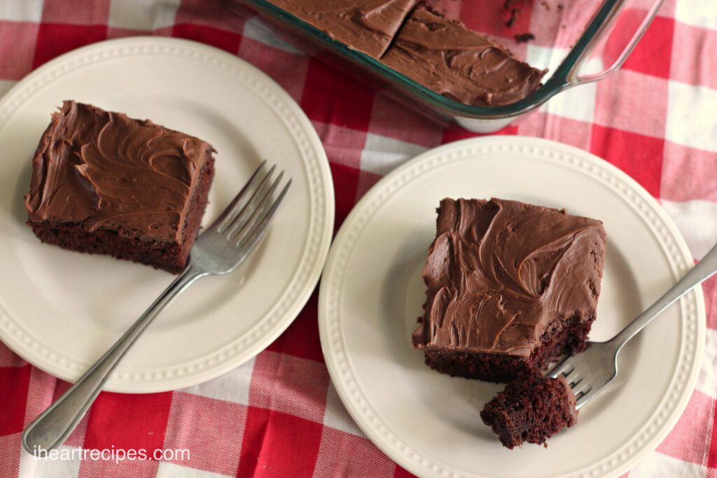 Slices of yummy sour cream chocolate take topped with a homemade chocolate frosting, served on white plates with silver forks.