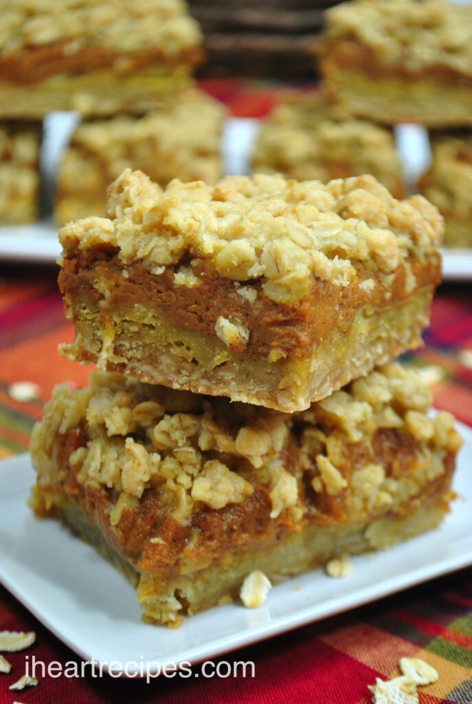 A close up look at two stacked homemade pumpkin pie bars and their distinctive layers of pie crust, spiced pumpkin filling, and a crumble topping.