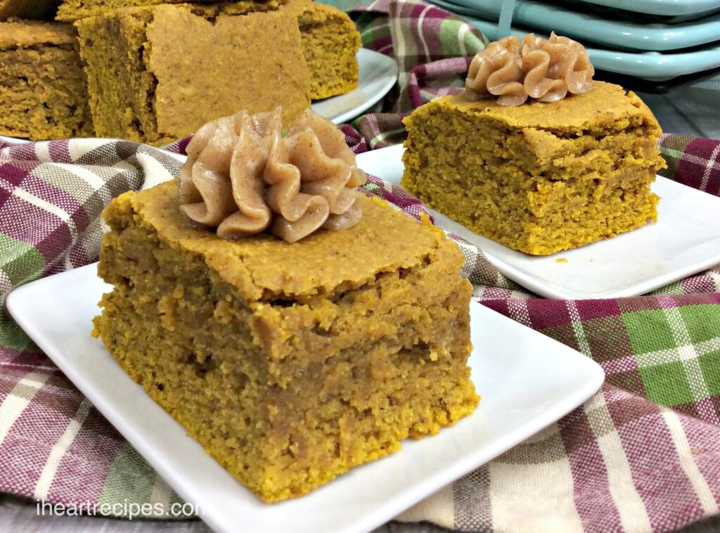 Two slices of deliciously moist pumpkin cornbread, topped with a dollop of a homemade spiced honey butter, served on small white ceramic plates.