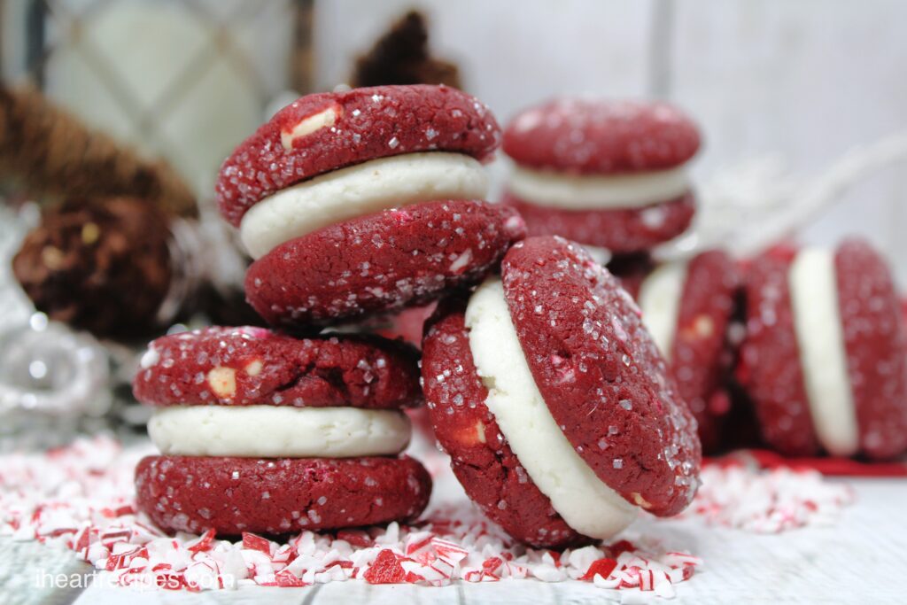 Homemade red velvet cookie sandwiches with a sweet cream filling and topped with coarse sugar and crushed peppermint candies.