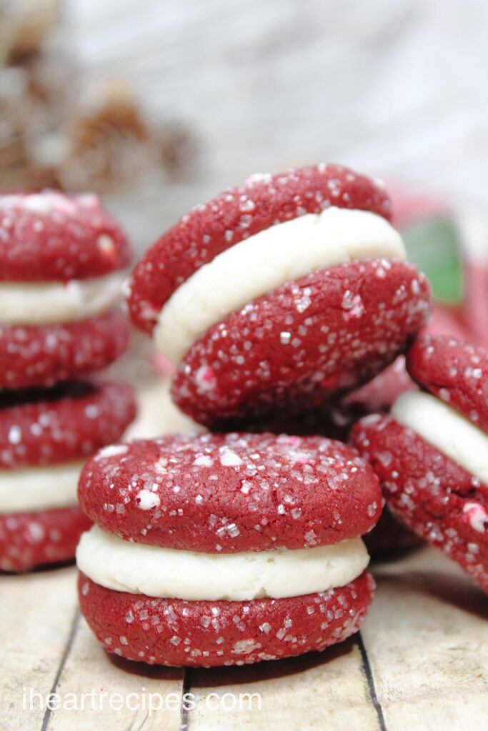 Stacks of homemade red velvet cookie sandwiches filled with a sweet cream, and topped with coarse sugar and crushed peppermint candies.