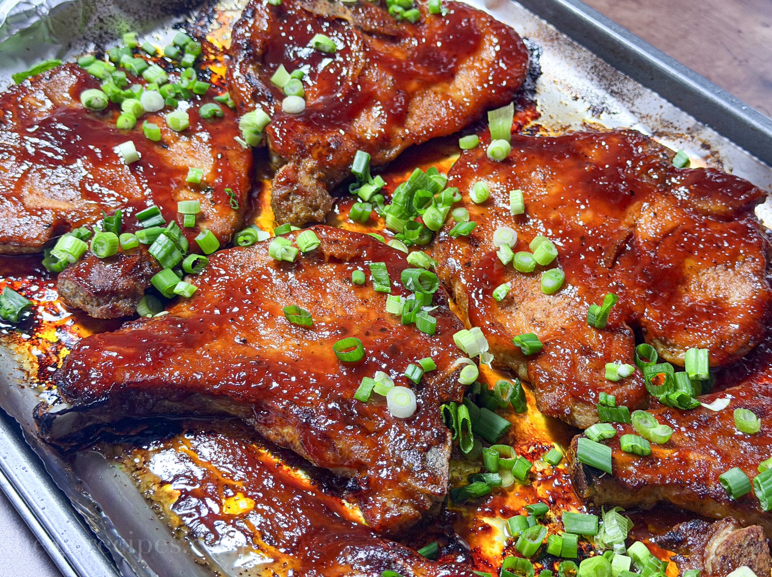 Oven baked pork chops on a baking sheet, sprinkled with green onions.