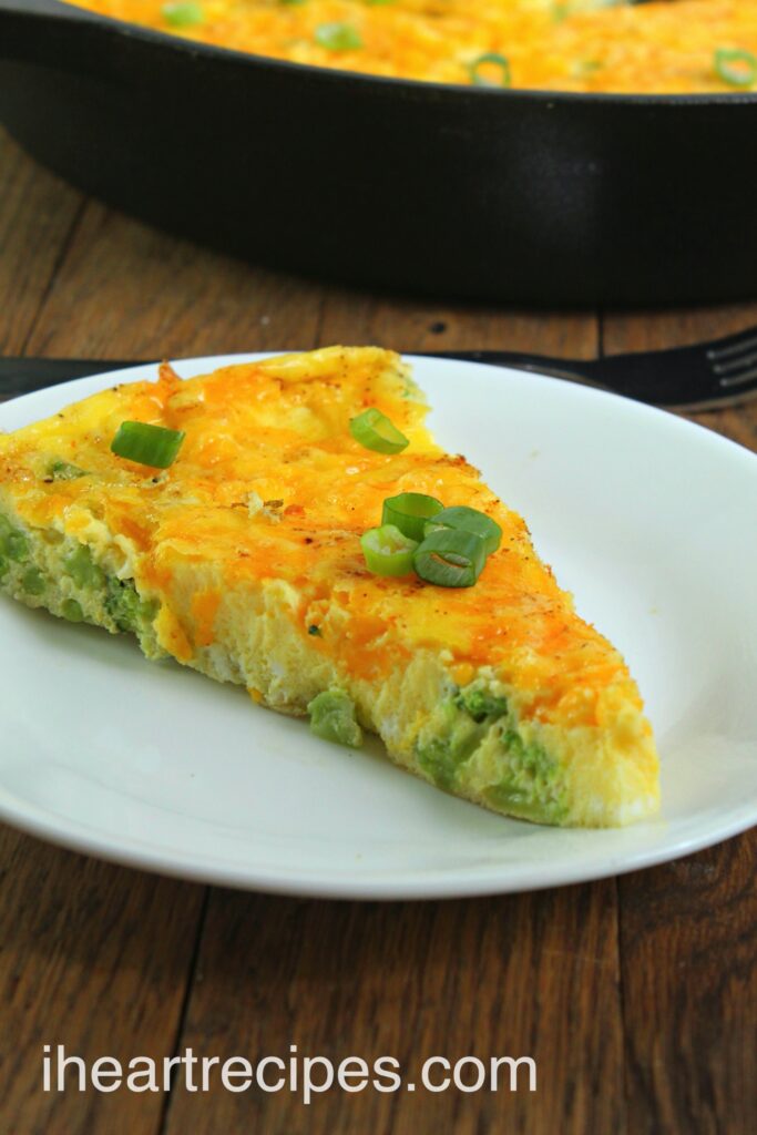 A slice of homemade breakfast frittata made with eggs, broccoli, and cheddar cheese, topped with green onions.
