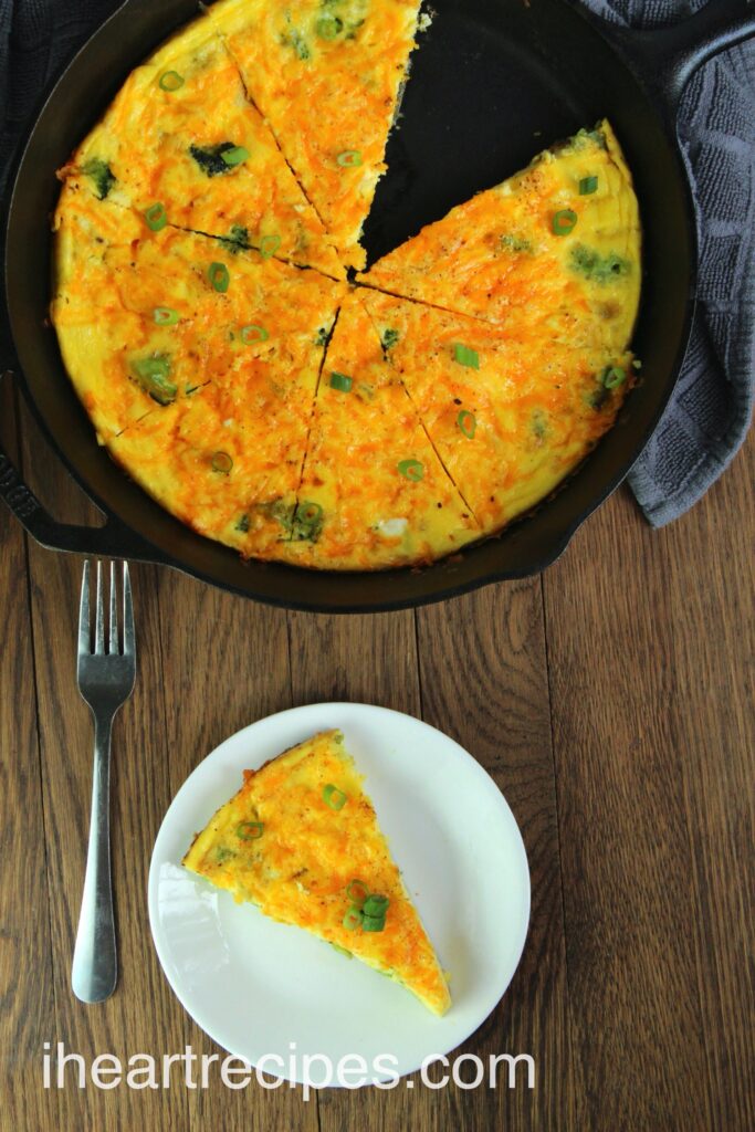 A cast iron skillet holds a egg, cheddar and broccoli frittata cut into 7 slices. A single slice of breakfast frittata sits on a white plate with a silver fork.