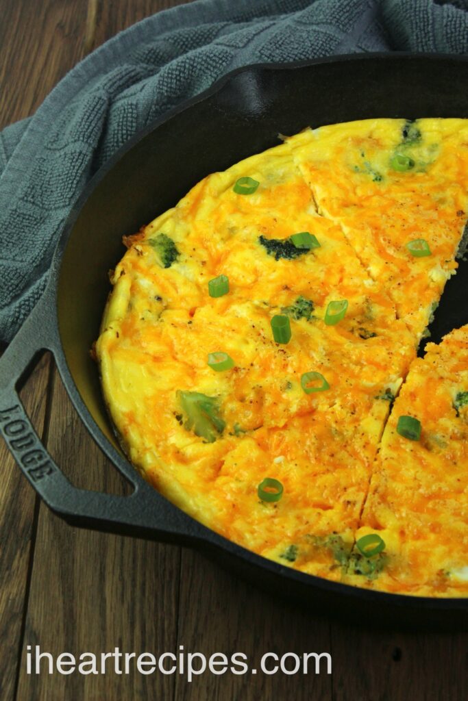 A large cast iron skillet with an egg, cheddar cheese and broccoli frittata topped with green onions.