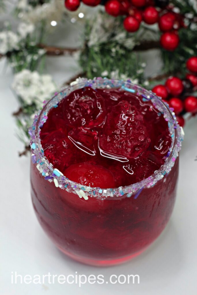 A perfectly Christmas cocktail made with cherry vodka, gin, fruit punch, and Sprite. The cocktail has a deep red color and is garnished with a sugar sprinkle rim.