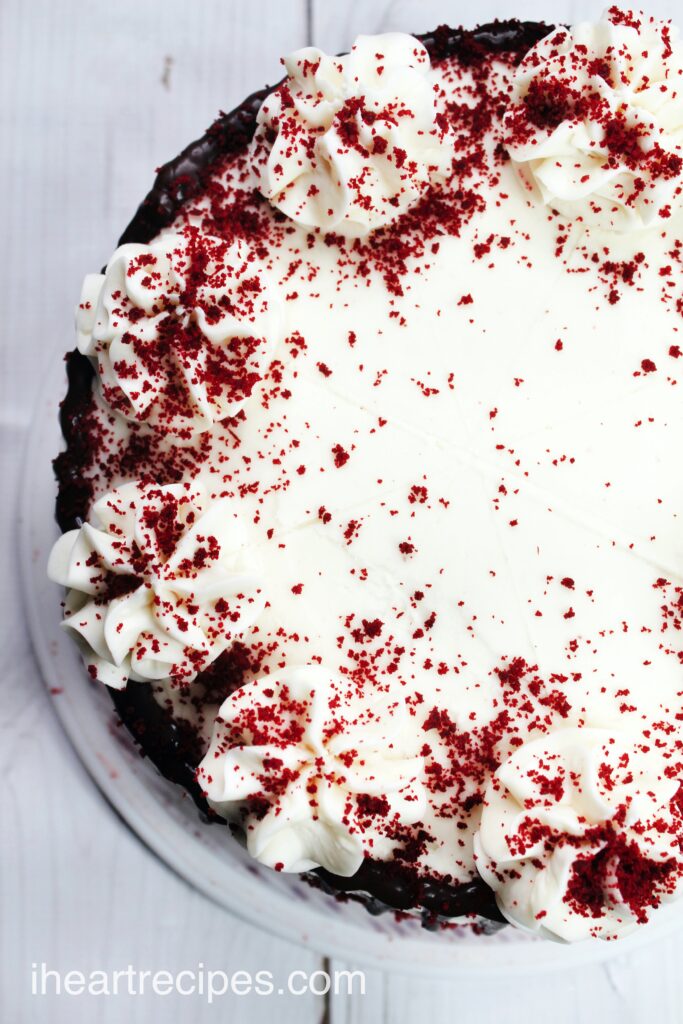 The decorated top of a 9-inch round red velvet cheesecake, iced with cream cheese frosting and sprinkled with red velvet cake crumbles.