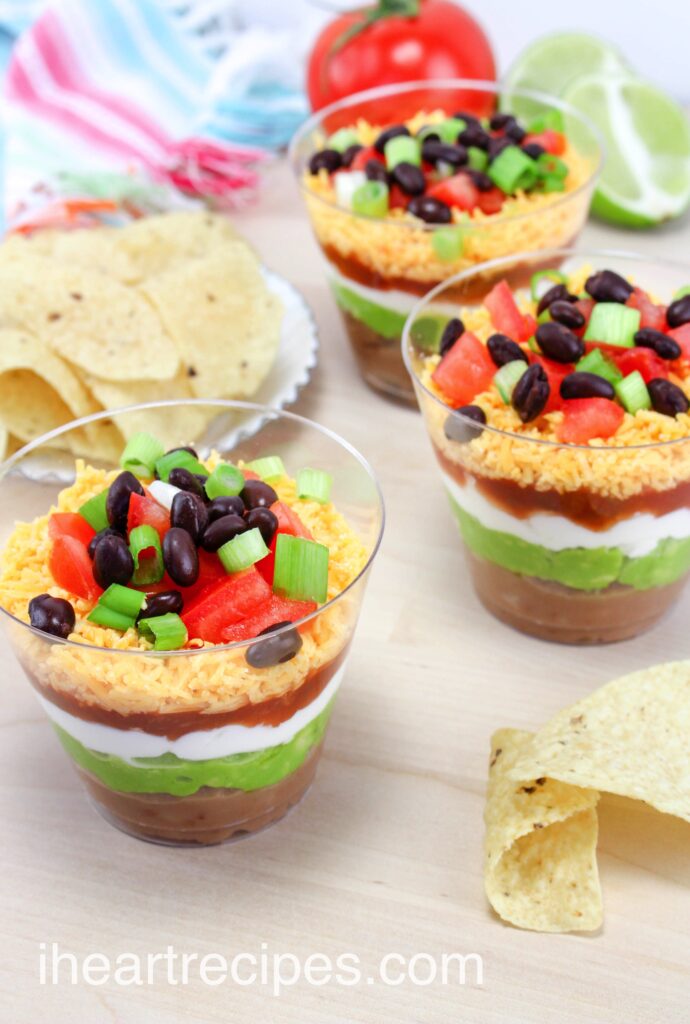 Individual nacho layer dip cups are perfect party appetizers. These small cups contain layers of cheese, salsa, sour cream guacamole, and refried beans.