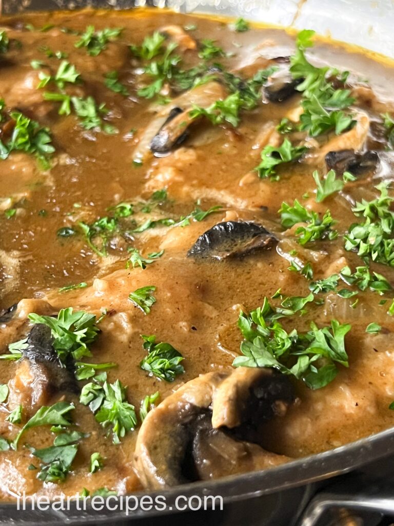 Skillet smothered pork chops in a rich brown mushroom gravy, garnished with fresh parsley leaves.