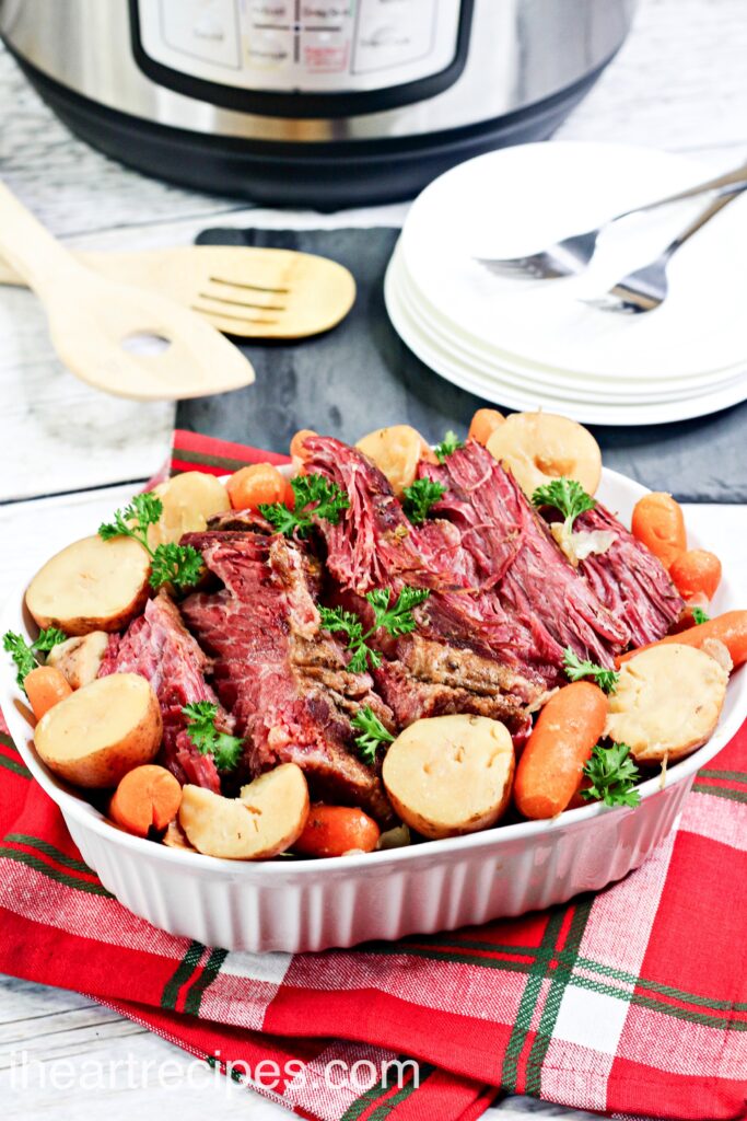 A casserole dish filled with cooked and sliced corned beef brisket, along with cooked potatoes, carrots, and cabbage.