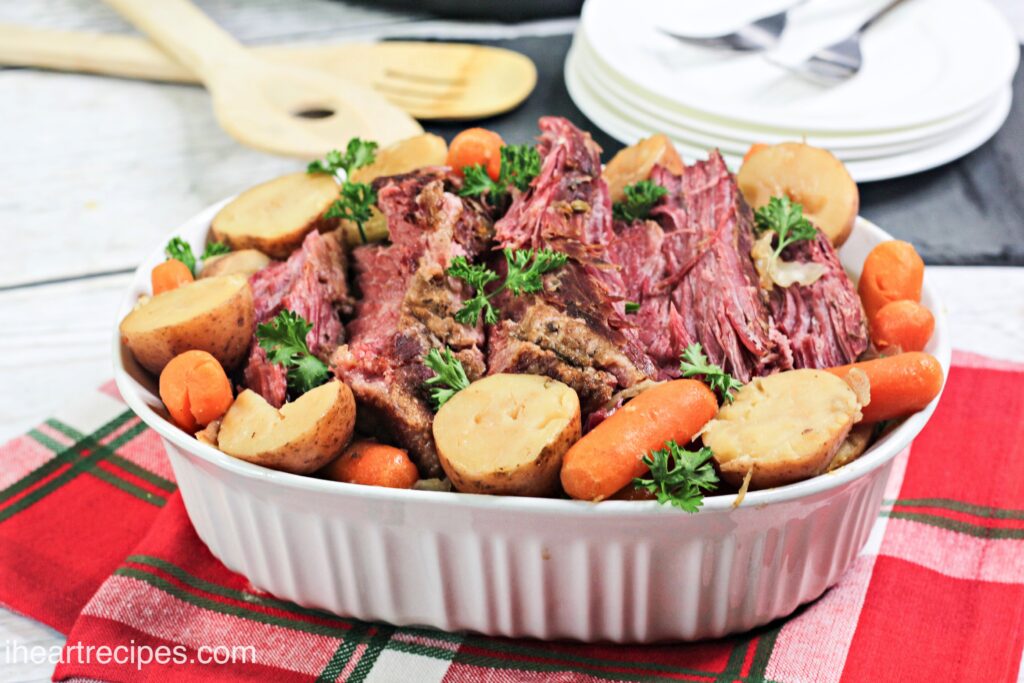 A large casserole dish is filled with sliced corned beef brisket surrounded by halved potatoes and baby carrots.