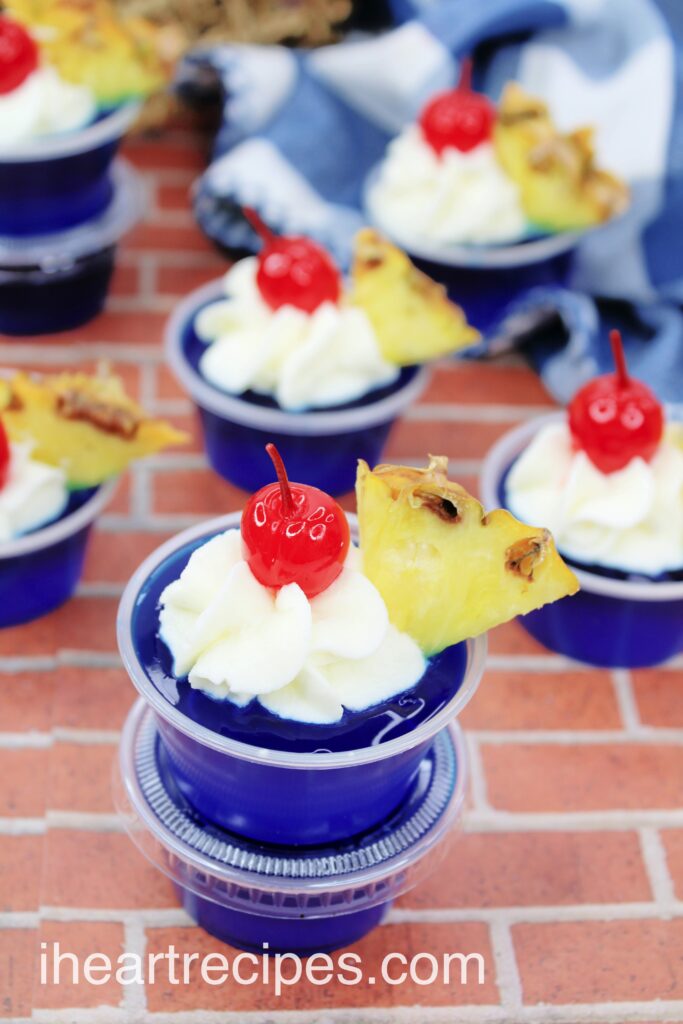 An overhead image of tropical Malibu Breeze Jello shots -- little cups of blue jello with whipped cream, cherries, and pineapple.