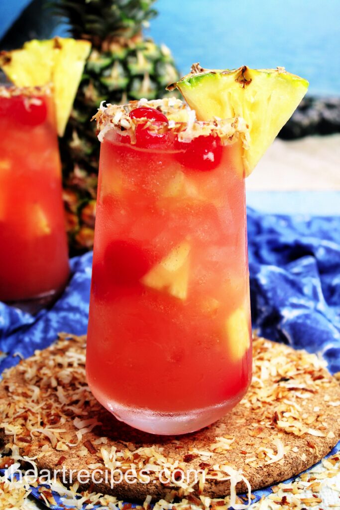 A close up image of a glass of Piña Colada sangria, garnished with pineapple, cherries, and toasted coconut flakes.