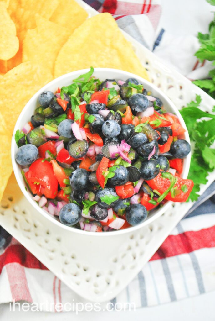 An overhead image of a bowl of fresh blueberry salsa served with yellow corn tortilla chips.