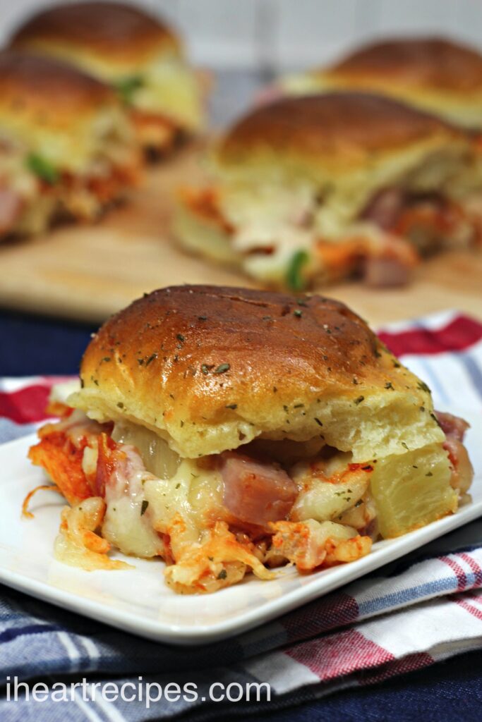 A single pizza slider, made with pizza sauce and cheese, and Canadian bacon, pineapple, and cheese. The toasted slider bun is topped with butter and herbs.