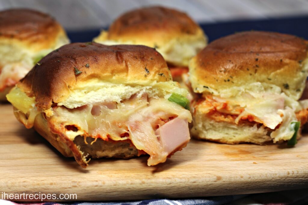 Four Canadian bacon and pineapple pizza sliders, made with pizza sauce and swiss cheese on slider rolls.