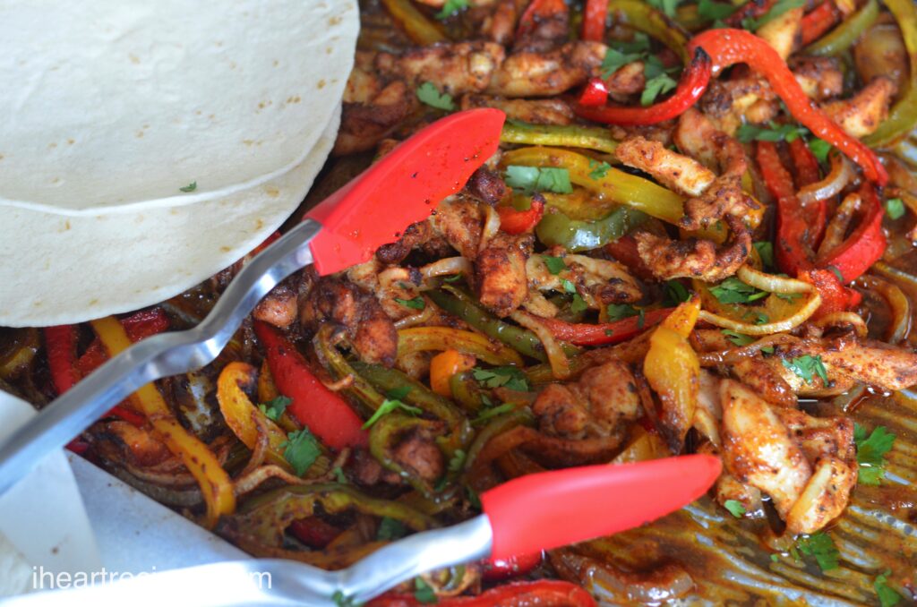 A sheet pan of chicken fajita ingredients  with tongs and flour tortillas, ready to assemble and enjoy!
