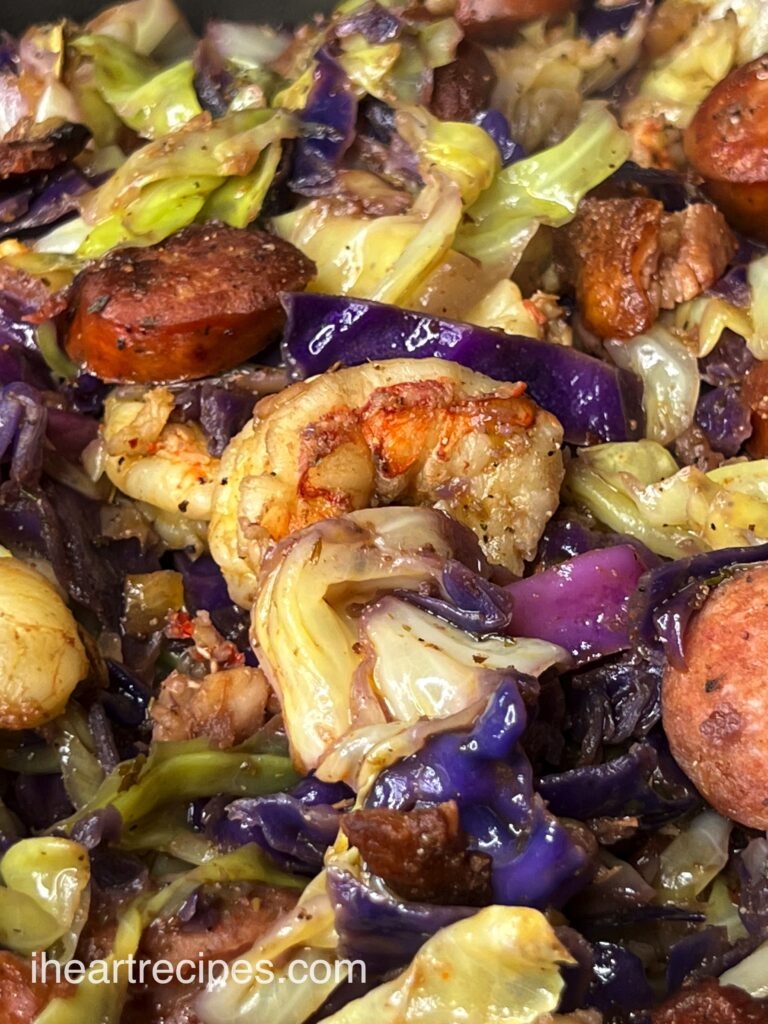 A close up image of red and green fried cabbage cooked with sausage, shrimp, and tons of Cajun seasoning.