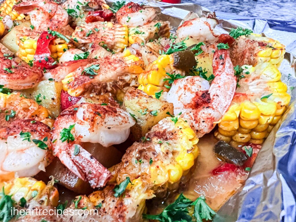 Ingredients for a one-pan shrimp boil -- shrimp, potatoes, corn on the cob, and seasonings -- spread out of a tin foil lined baking sheet.
