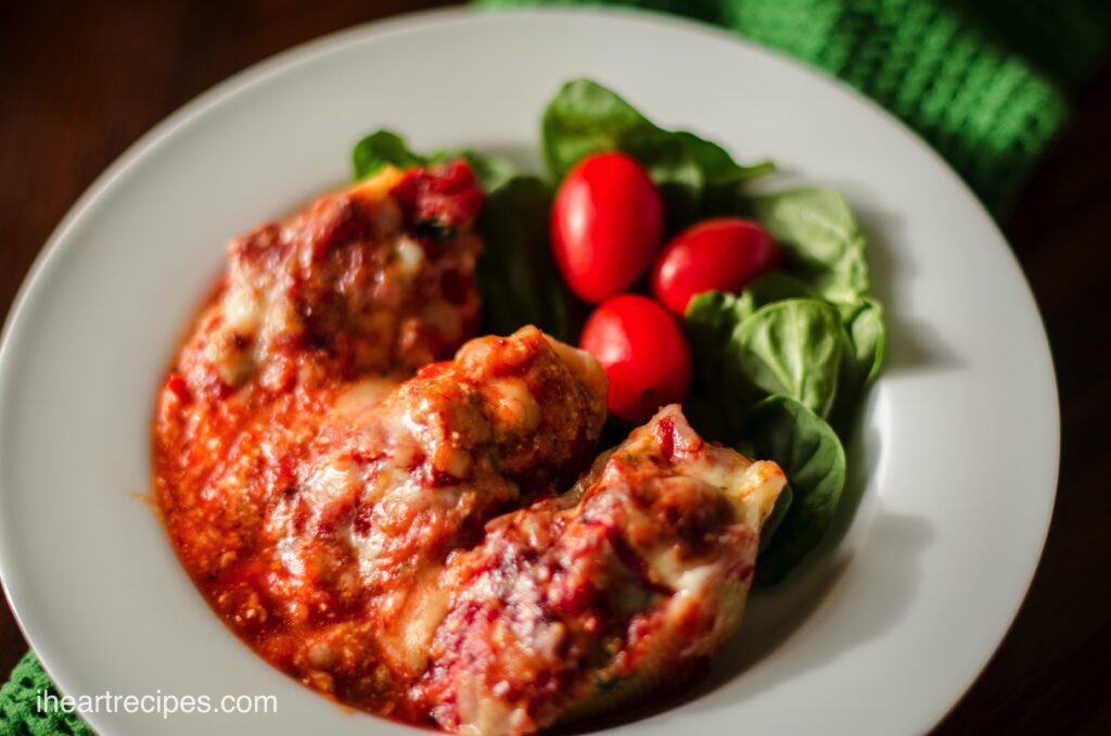 A bowl full of Italian style stuffed shells baked in a cheesy meat sauce, and served with a side salad of spinach and tomatoes.