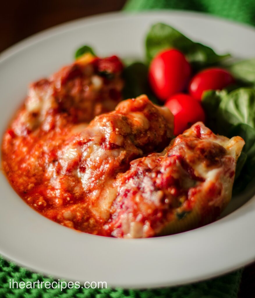 A closeup image of stuffed shells served with pasta sauce in a white bowl, with a spinach and tomato salad.