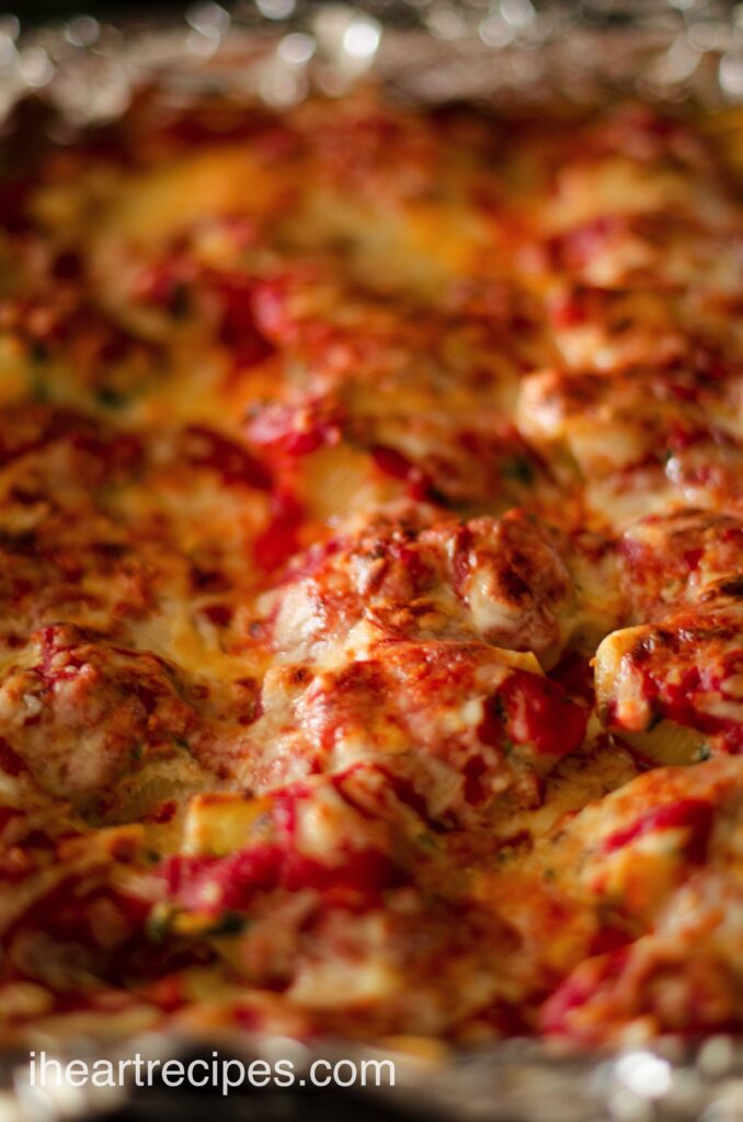 A closeup image of cheesy baked stuffed shells served in a casserole dish.