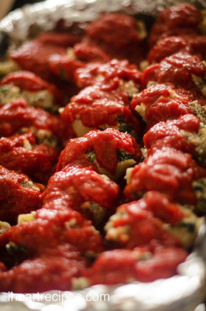 Stuffed shells lined up in a baking dish, filled with a cheesy spinach mixture and topped with pasta sauce.