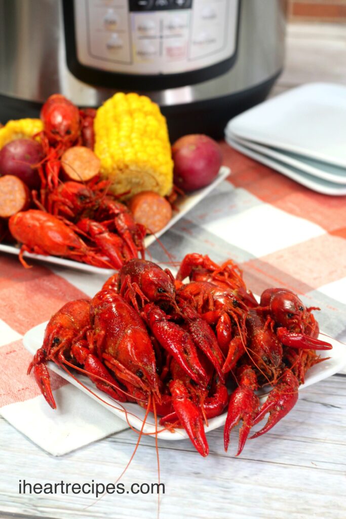 Two plates of cooked crawfish, boiled in an Instant Pot. The second plate of seafood is also served with andouille sausage, red potatoes, and corn on the cob.