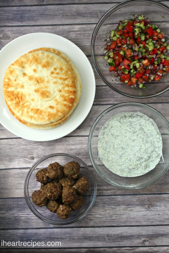 An overhead image of some of the ingredients needed to make meatball gyros -- pita bread, Greek style meatballs, a fresh cucumber pico, and homemade tzatziki sauce.