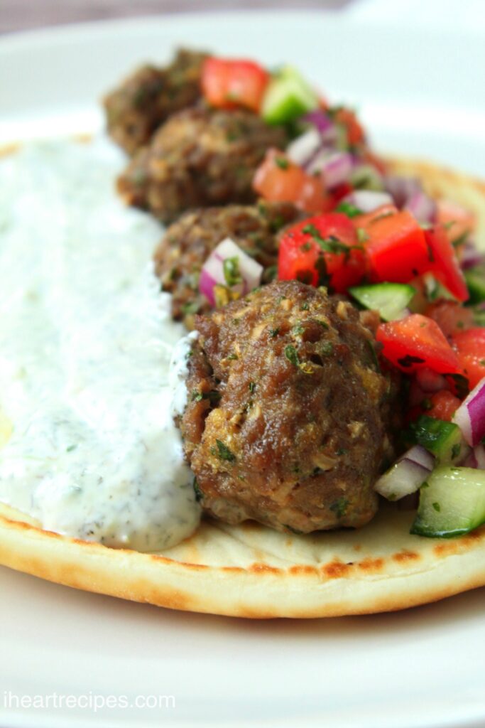 A closeup image of a meatball gyro made with a cucumber tomato salad and homemade Tzatziki sauce on pita bread.