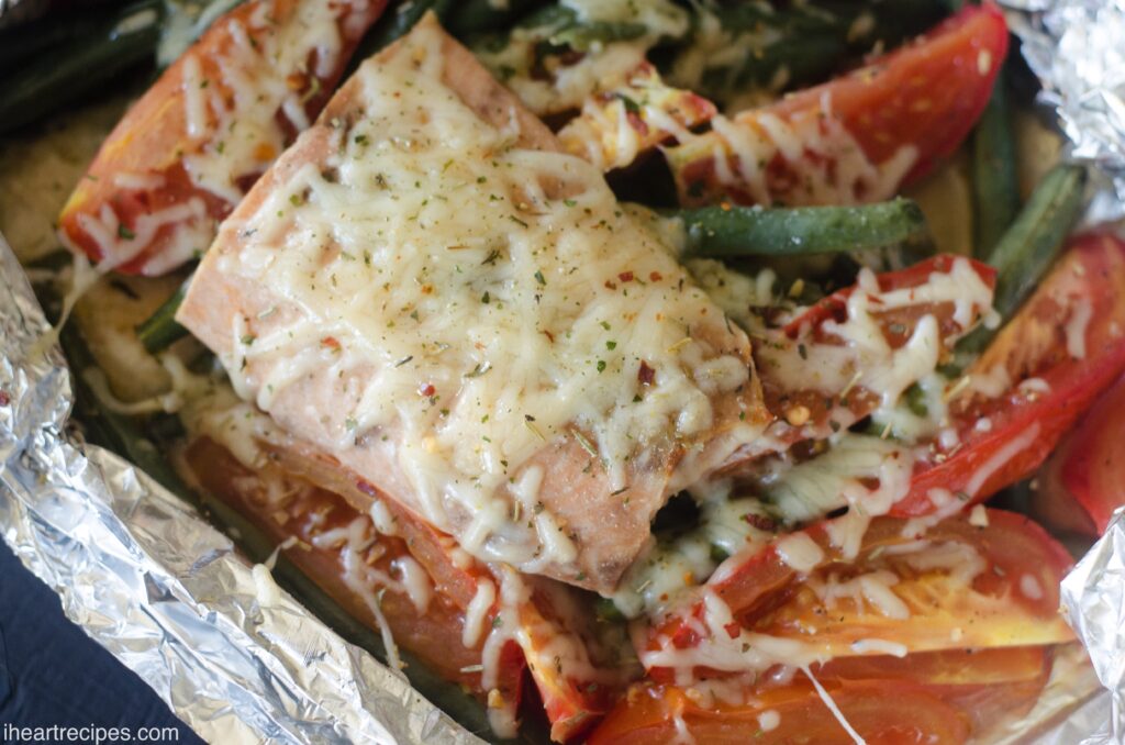 Cheesy Parmesan salmon baked on top of sliced vegetables in a foil packet.