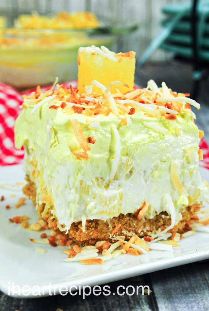 A close up image of a slice of no bake pina colada cheesecake, topped with crunchy toasted coconut and a pineapple square.