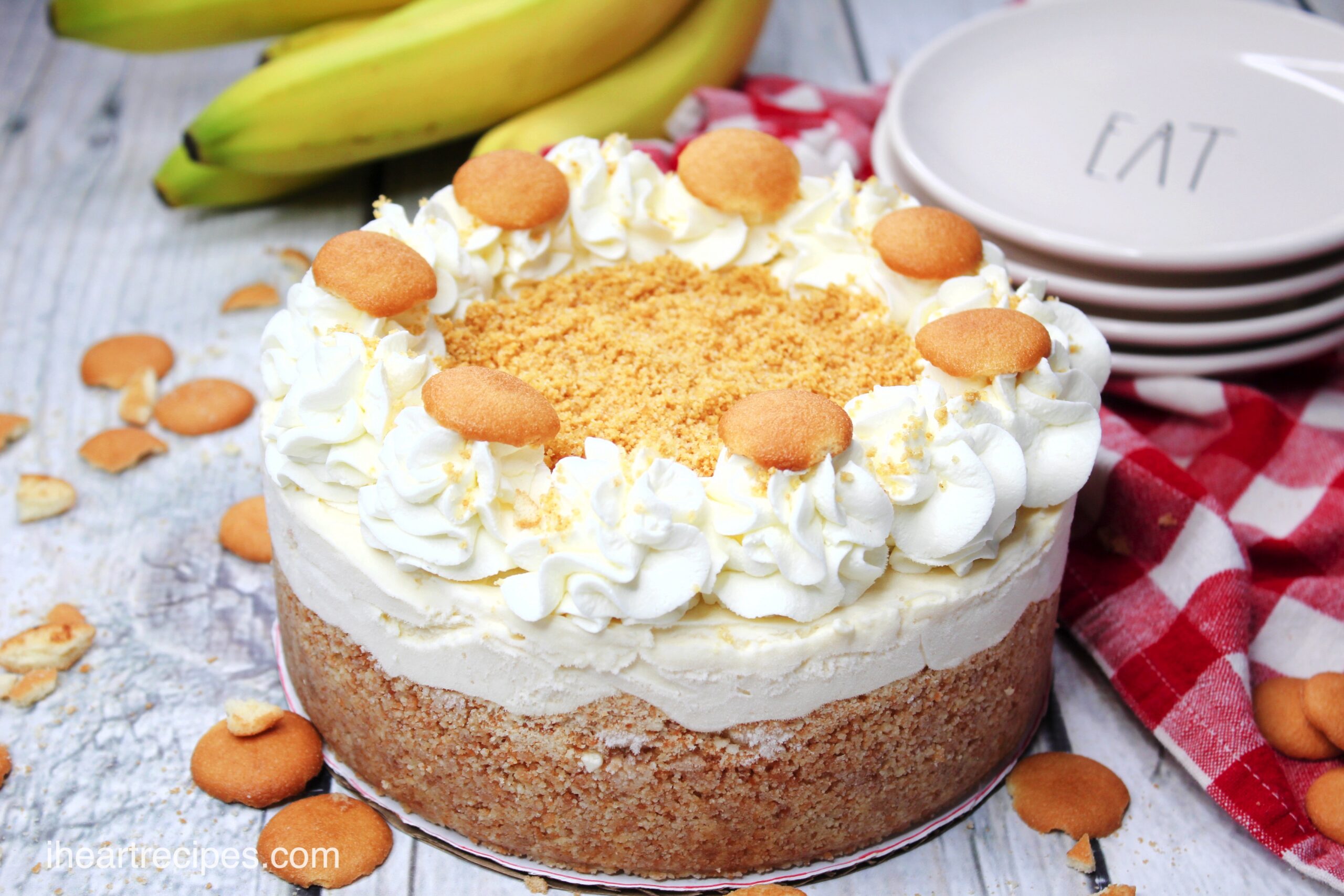 A whole banana pudding cheesecake, topped with whipped cream and vanilla wafers. The cheesecake has layers of wafer crust, banana pudding, and whipped cream.