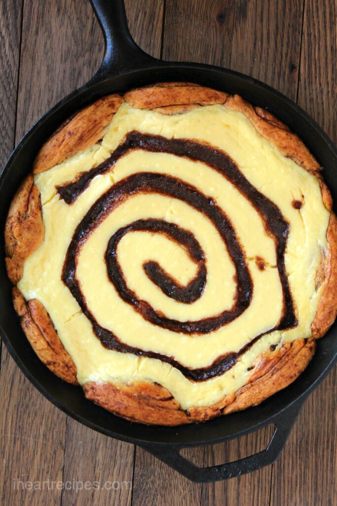 An overhead image of a cinnamon roll cheesecake, baked in a cast iron skillet with a cinnamon swirl cheesecake filling.