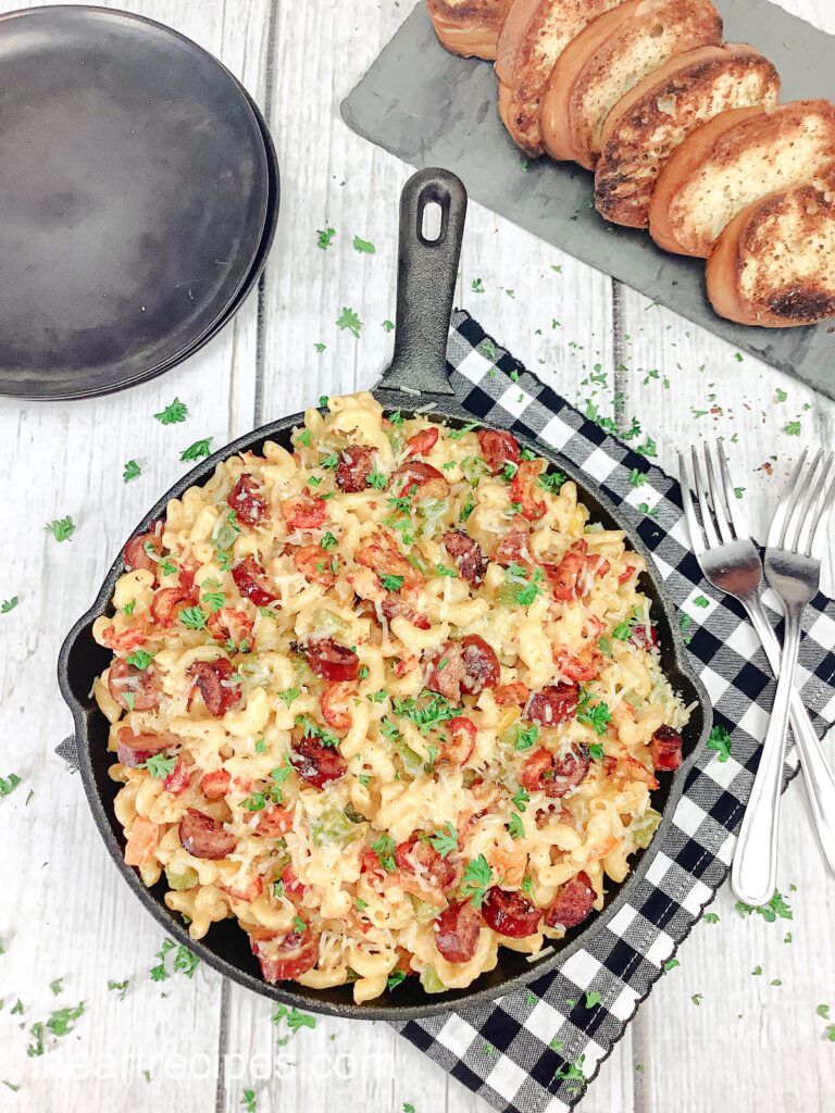 An overhead image of a cast iron skillet of mac and cheese with crawfish and andouille sausage topped with fresh parsley.