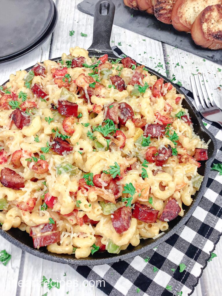 A close up image of Cajun mac and cheese served in a cast iron skillet, with flavorful pieces of crawfish and andouille sausage mixed in.