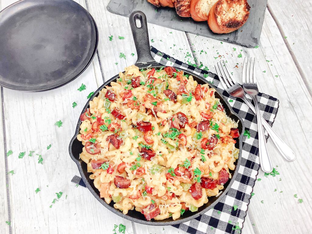 An overhead image of a cast iron skilled filled with crawfish mac and cheese, served on a black and white checkered napkin along with cristinis.