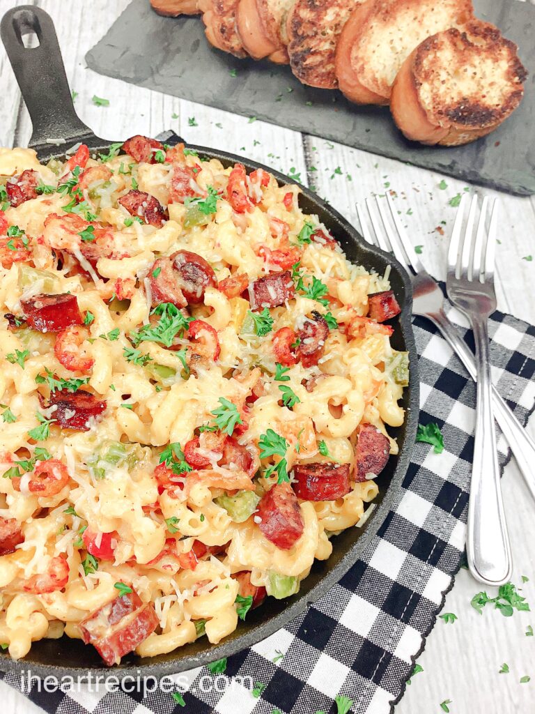 A cast iron skillet of crawfish mac and cheese served with two forks and a plate of garlic bread.